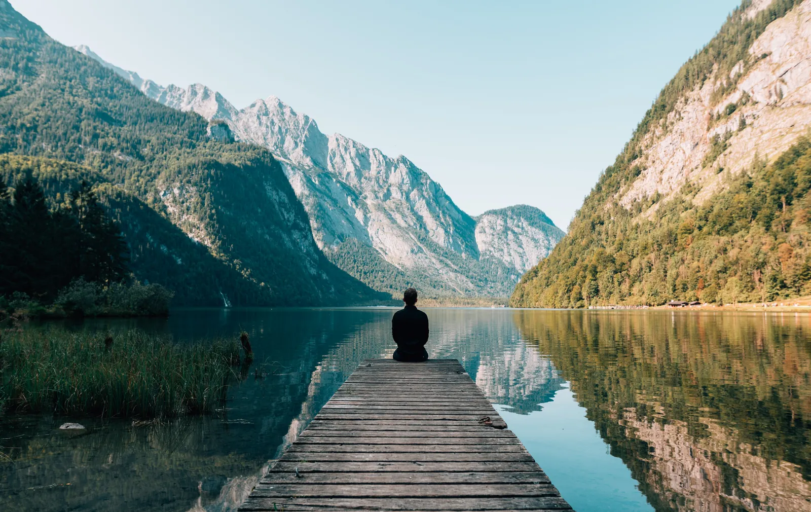 Personne assise au bout d'un ponton face à un lac de montagne